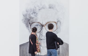 Man and woman walking past and looking at a mostly black and white painting of an eldery woman wearing brown glasses